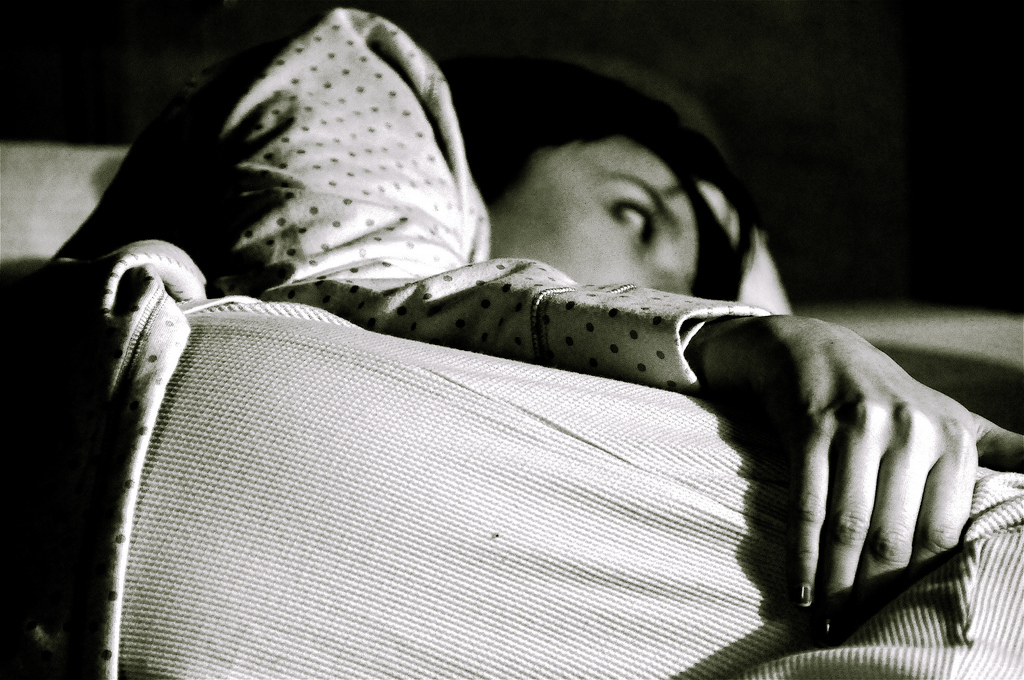 Schwarzweiss-Foto einer Frau, die wach im Bett liegt.