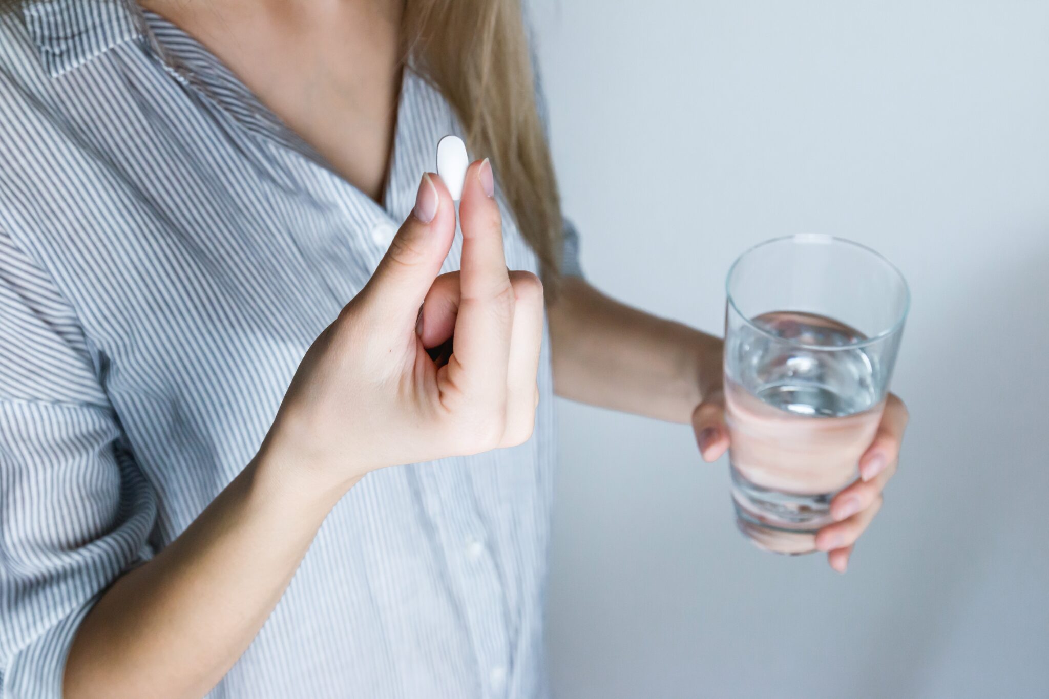 Frau mit Glas Wasser in linker Hand und Pille in der rechten Hand