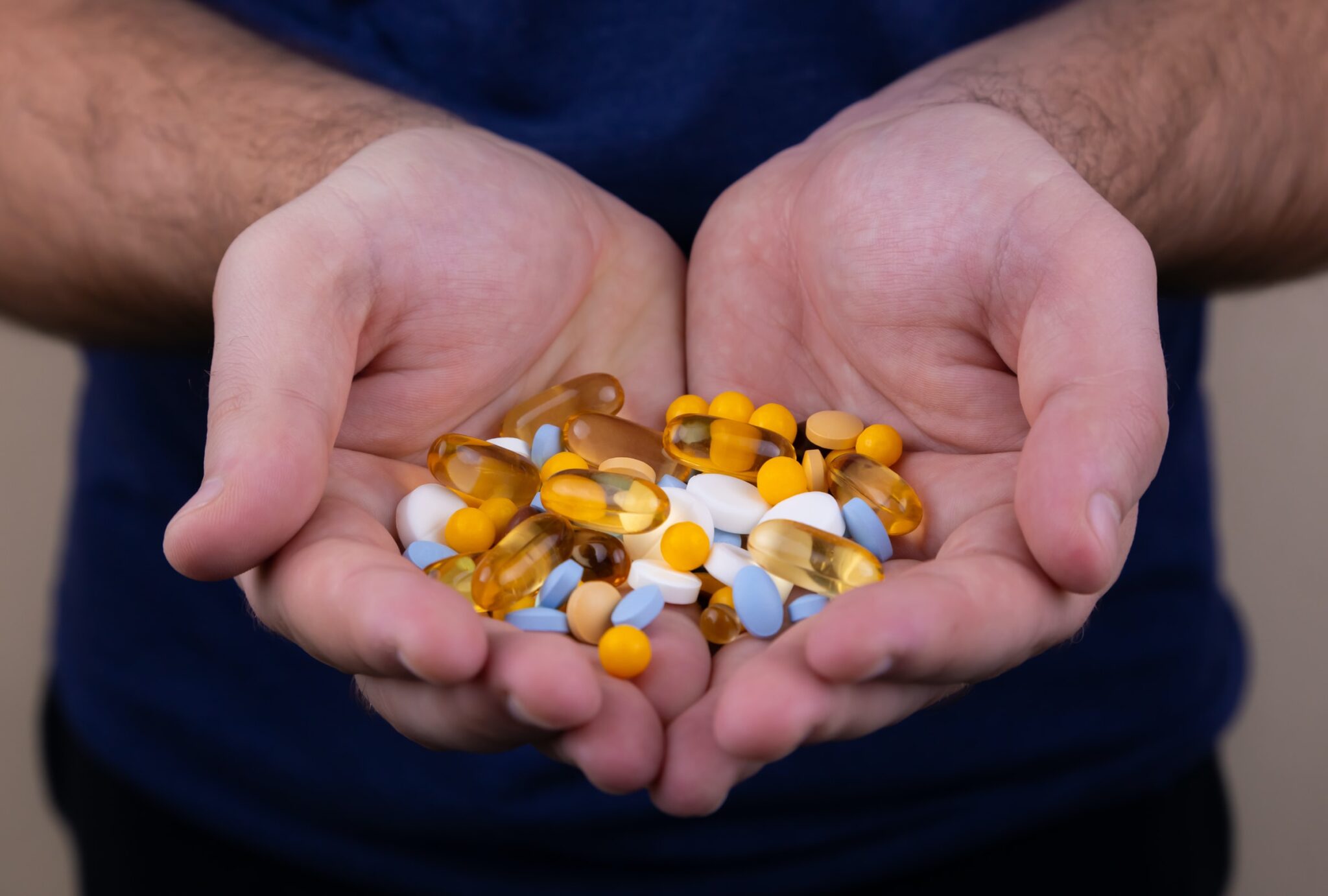 Verschiedenfarbige Pillen und Tabletten in 2 Händen, die aneinandergehalten werden.