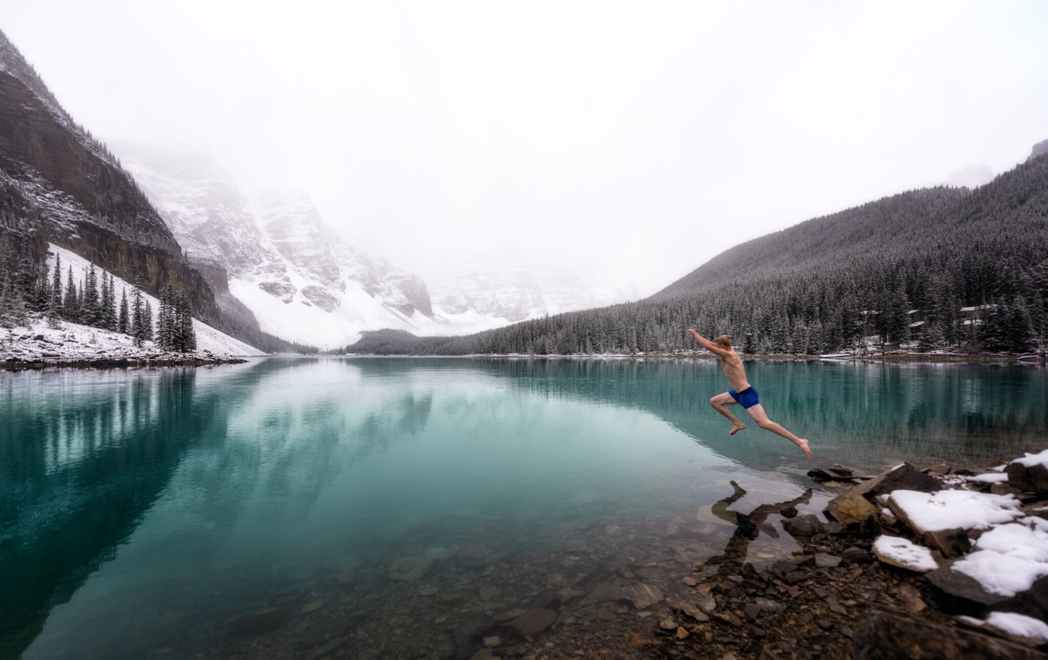 Ein Mann springt in einen kalten See in verschneiter Berglandschaft.