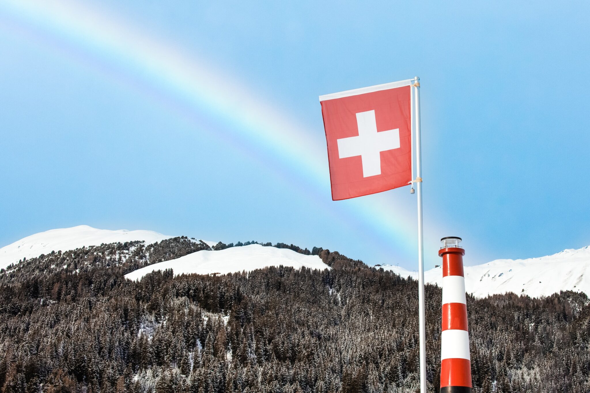Schweizer Flagge in den Bergen mit Regenbogen im Hintergrund.