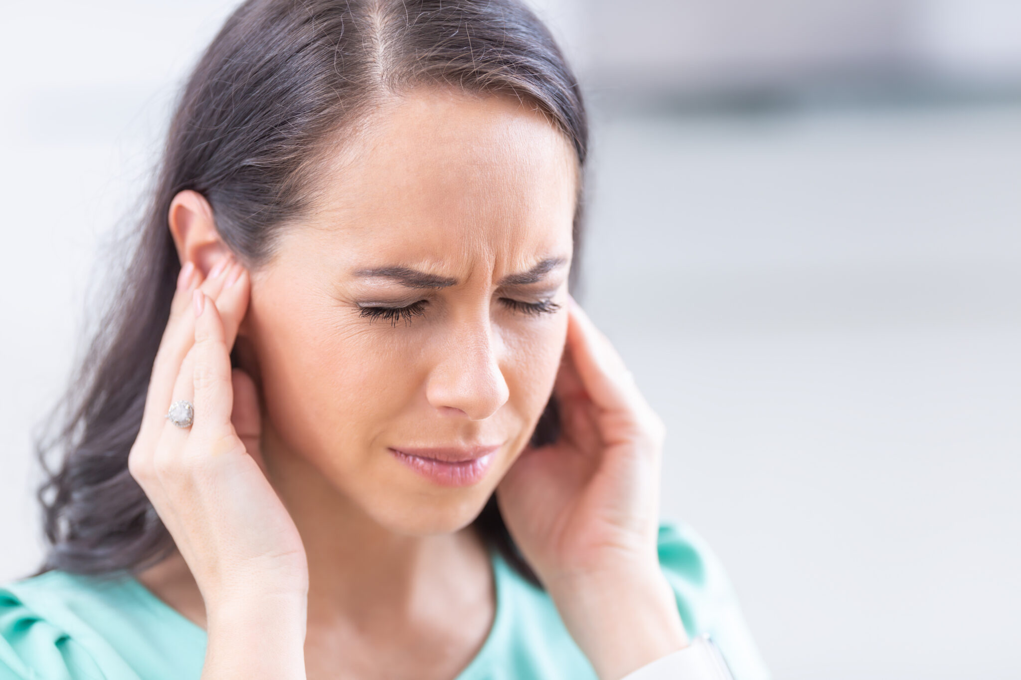 Eine Frau hält sich mit schmerzverzerrtem Gesicht die Ohren.