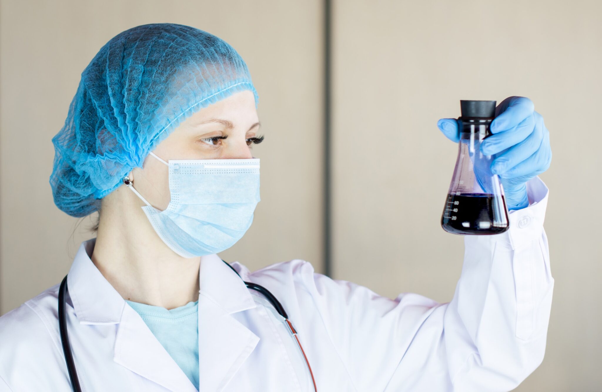 Eine Krankenpflegerin mit Maske und Haarnetz hält einen Kolben mit blauer Flüssigkeit.