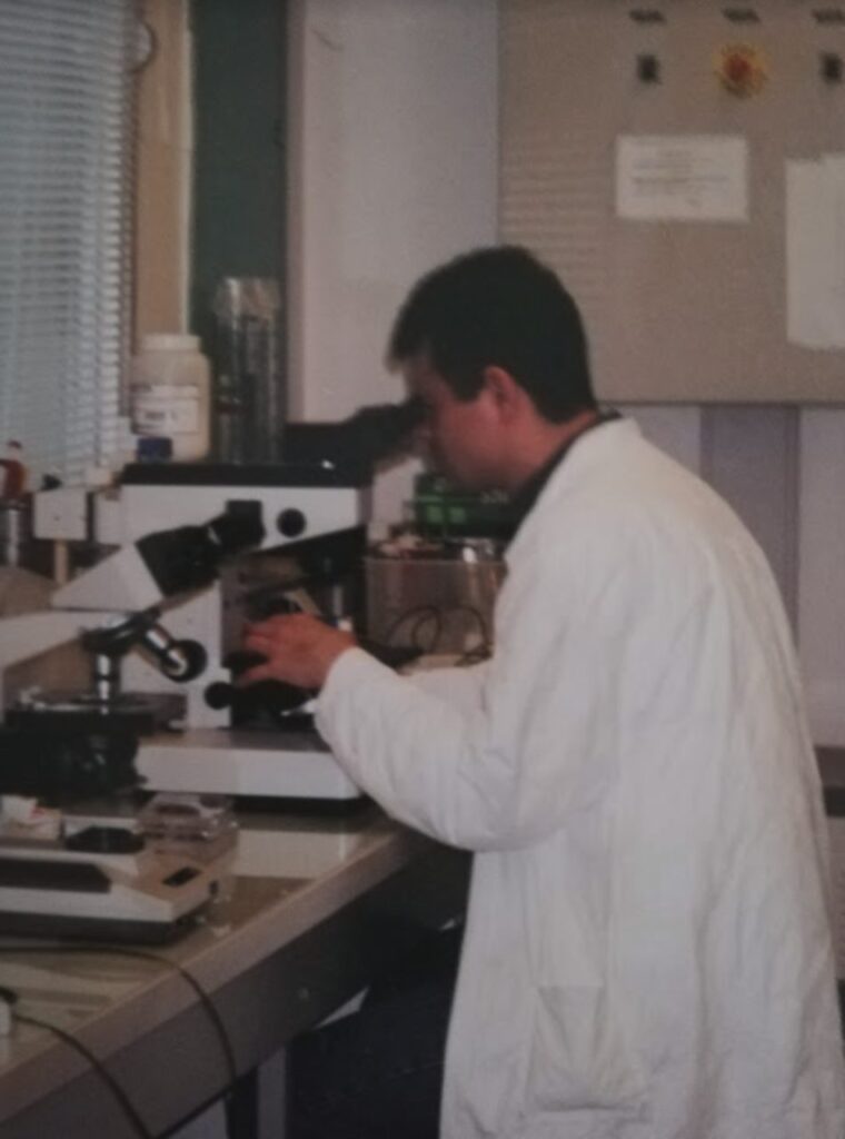 Ein Wissenschaftler schaut im Laborkittel durch ein Mikroskop