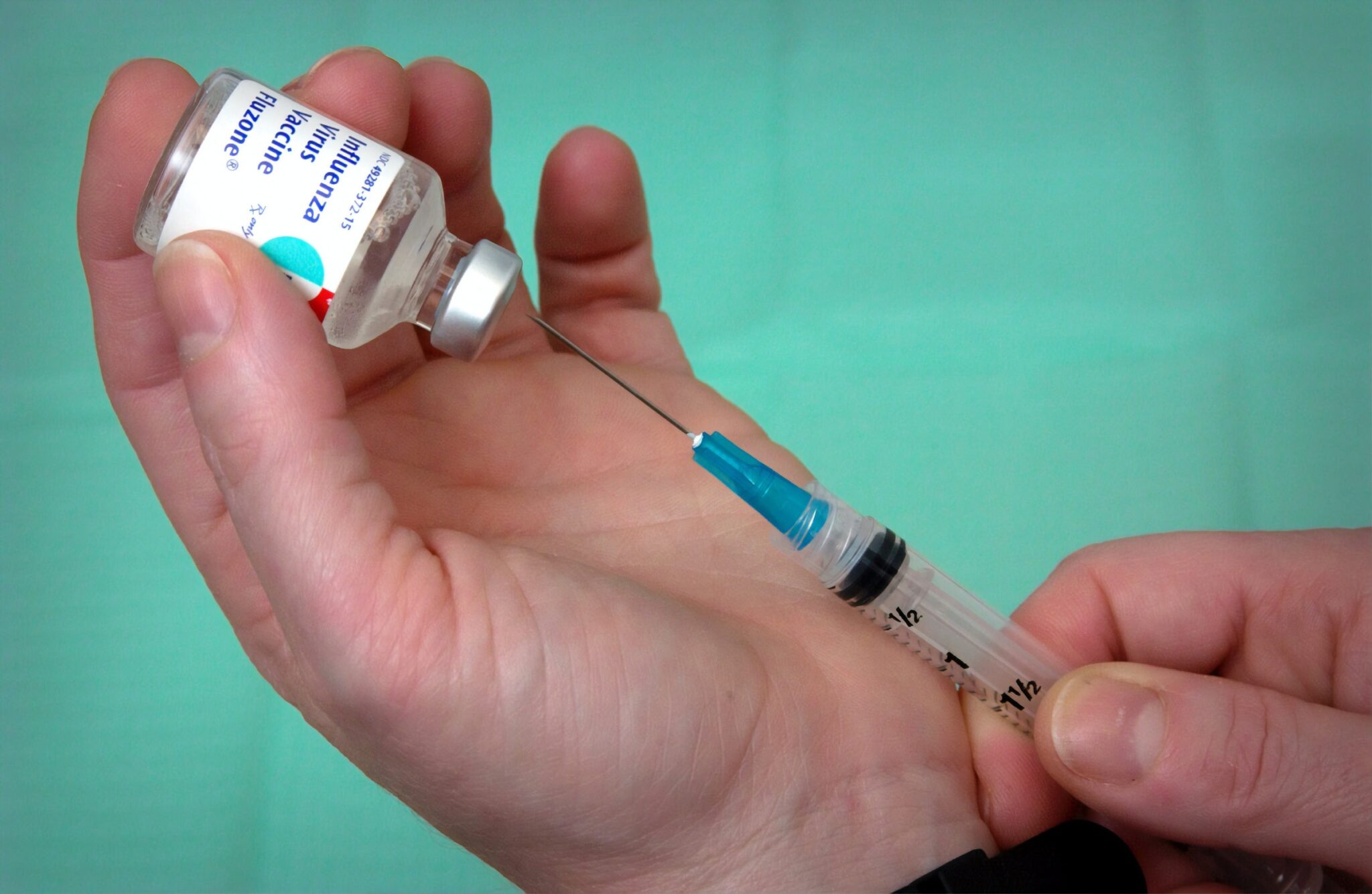 Nahaufnahme, wie eine Spritze kurz davor ist, in ein Fläschchen mit Grippe-Impfstoff gesteckt zu werden.