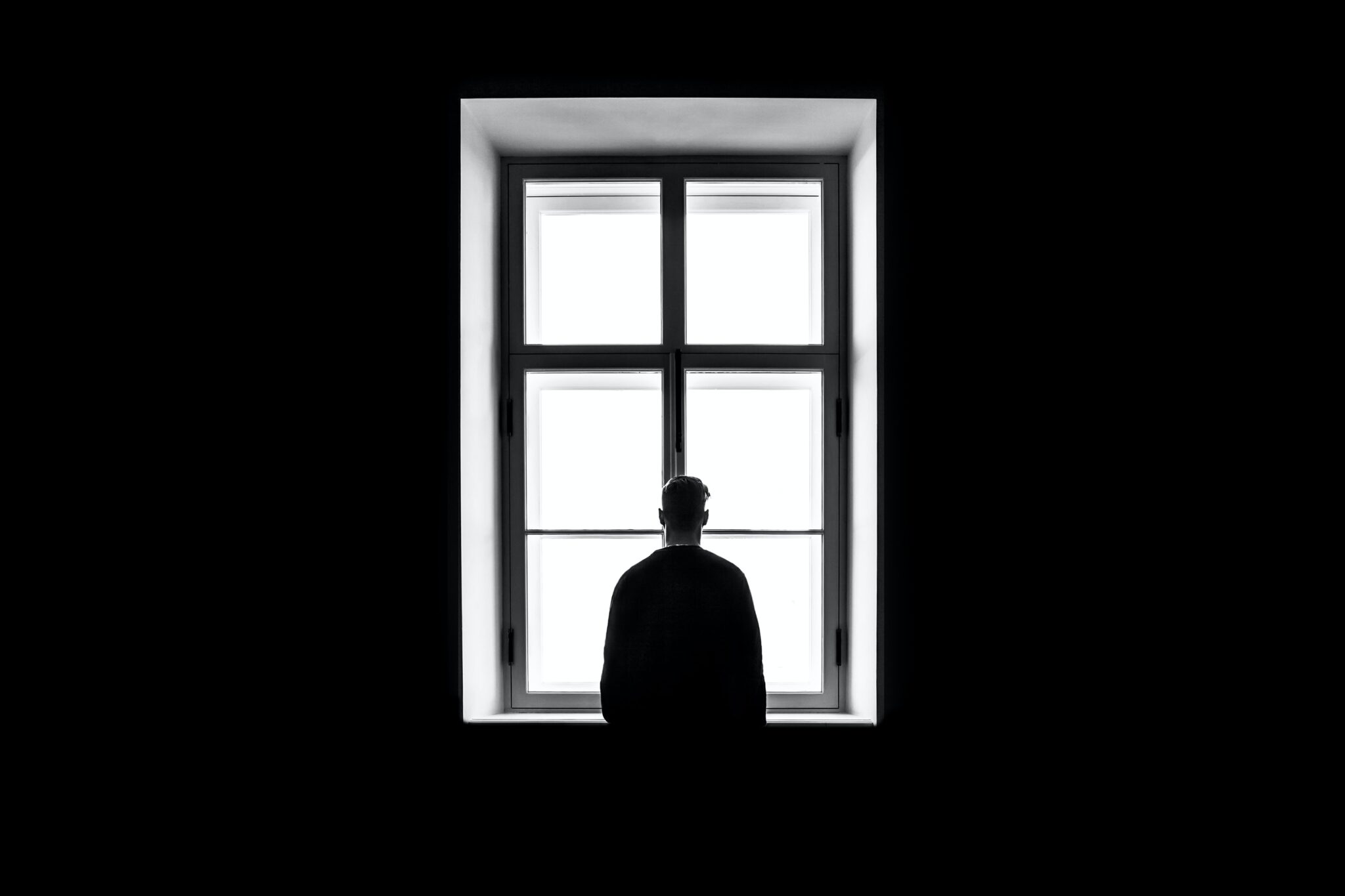 Schattenriss eines Mannes, den man von hinten sieht, wie er durch ein grosses Fenster nach draussen schaut.