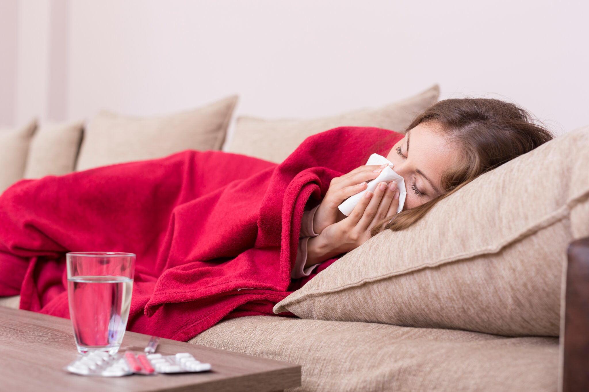 Eine Frau liegt mit Grippe auf der Couch und putzt sich die Nase