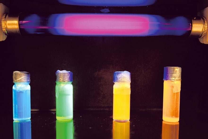 Röhrchen, die mit bunt leuchtenden Substanzen gefüllt sind: blau, grün, gelb, orange