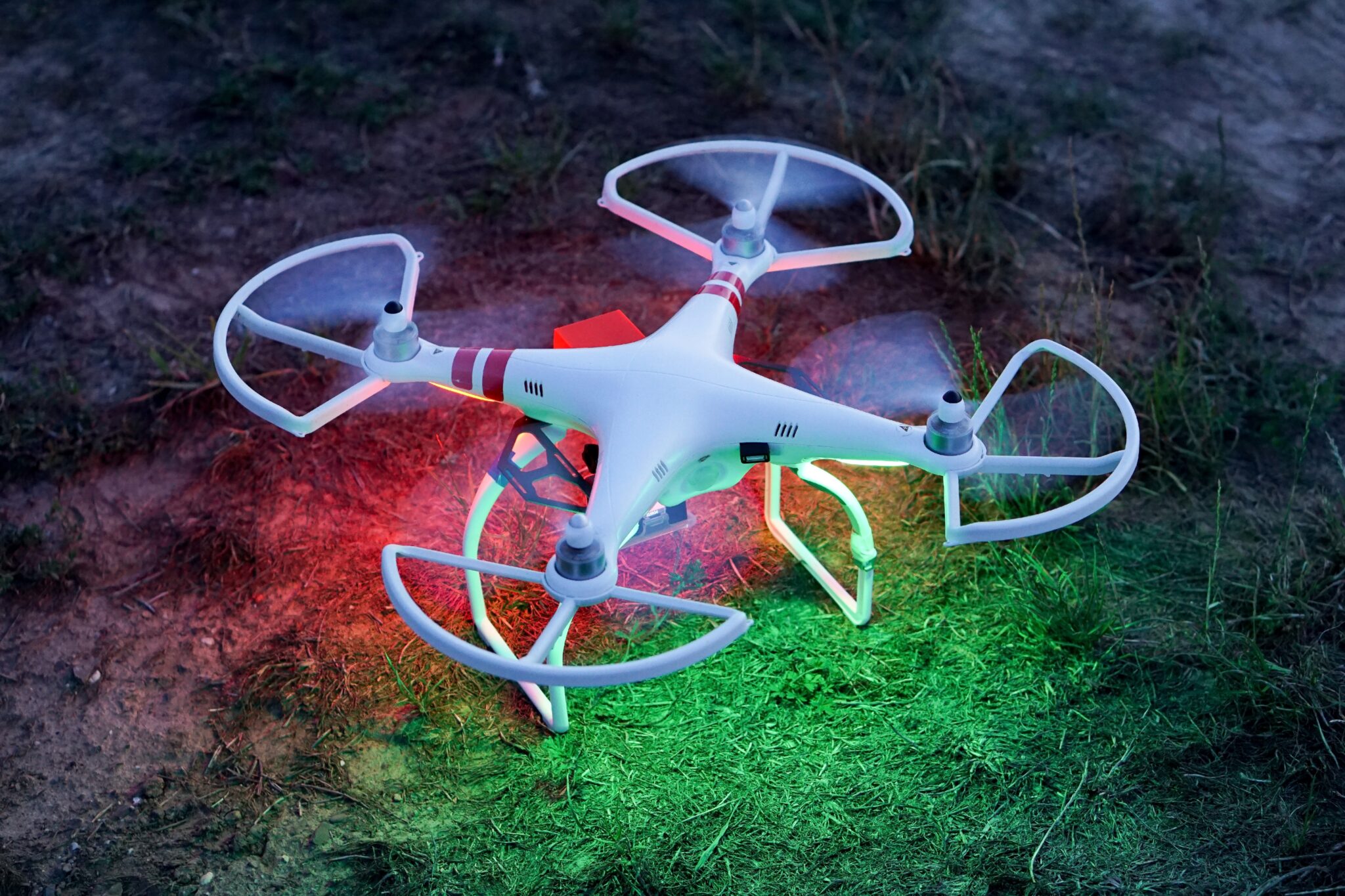 Eine weisse Drohne beleuchtet einen Ackerboden in rotem und grünem Licht.
