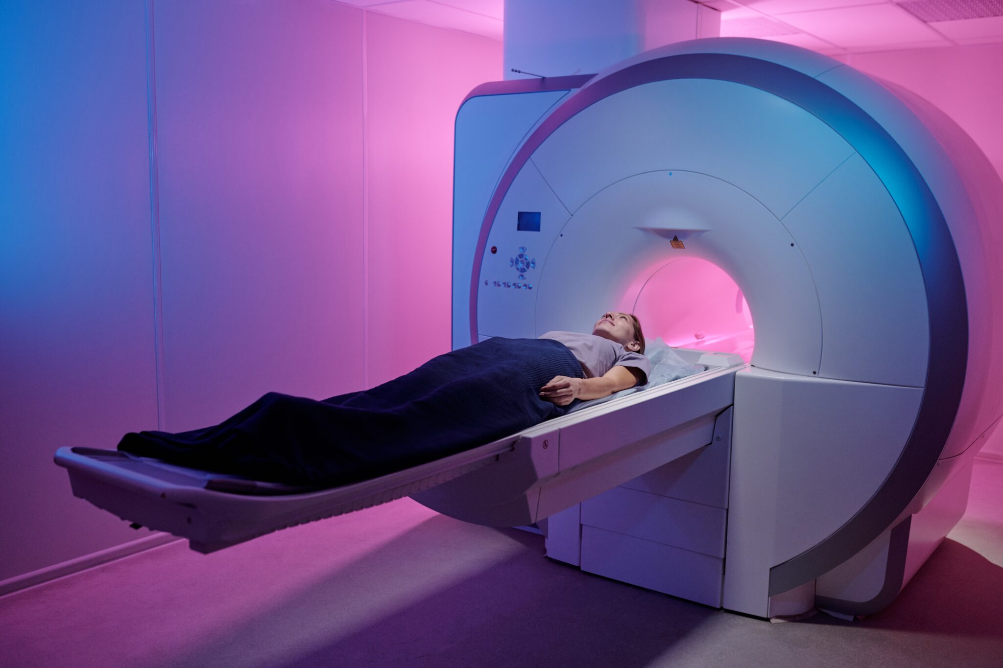 Eine Frau liegt vor einem Magnetresonanztomographen mit rosa Beleuchtung.