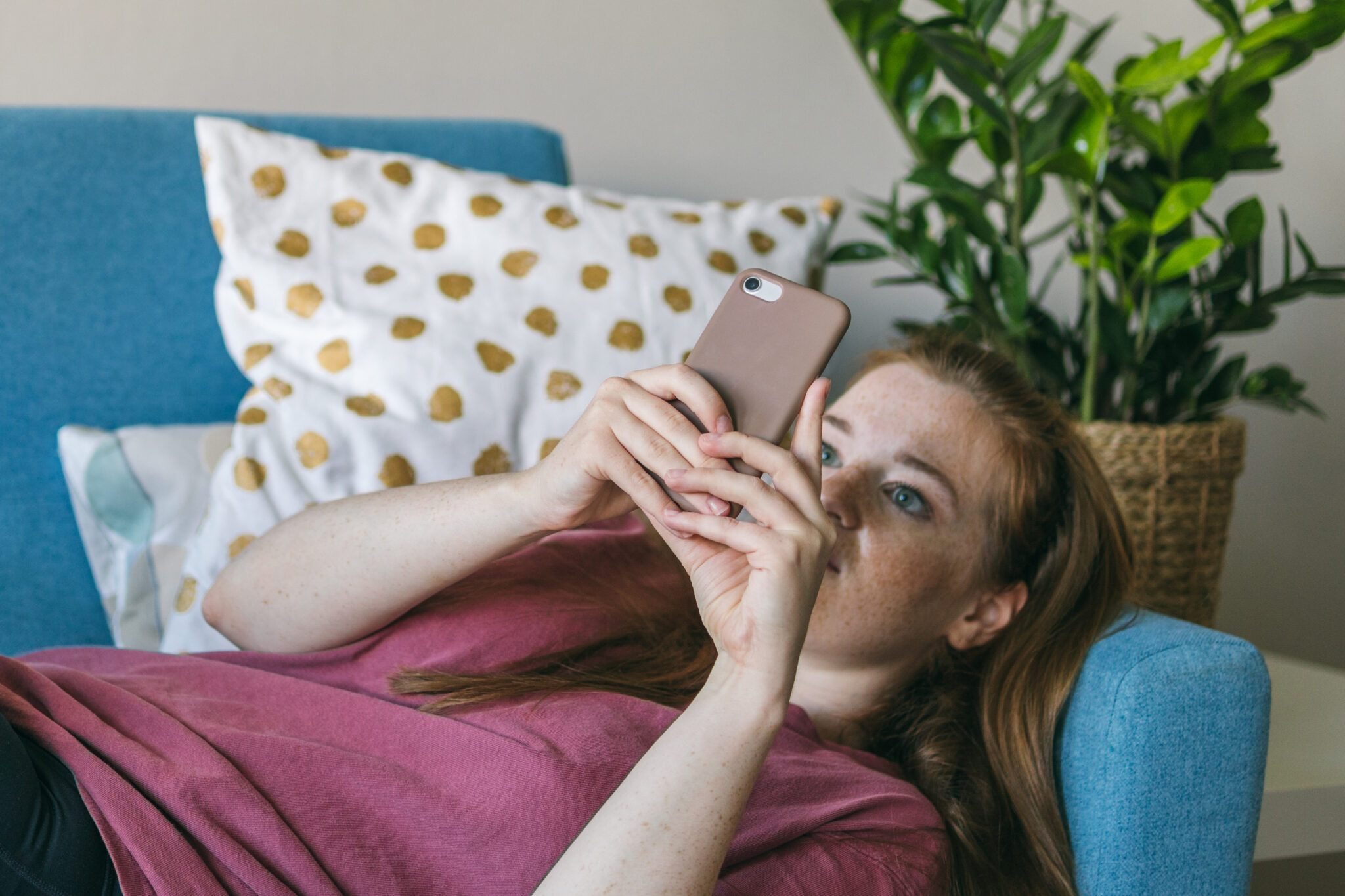 Eine junge Frau liegt auf der Couch und schaut in ihr Handy.