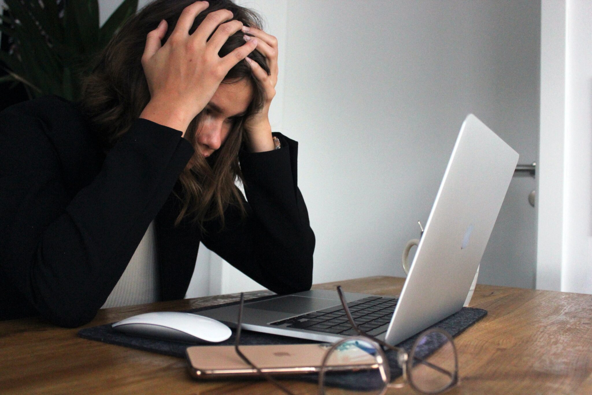 Eine Frau sitzt gestresst vor ihrem Laptop und hält sich den Kopf mit beiden Händen.