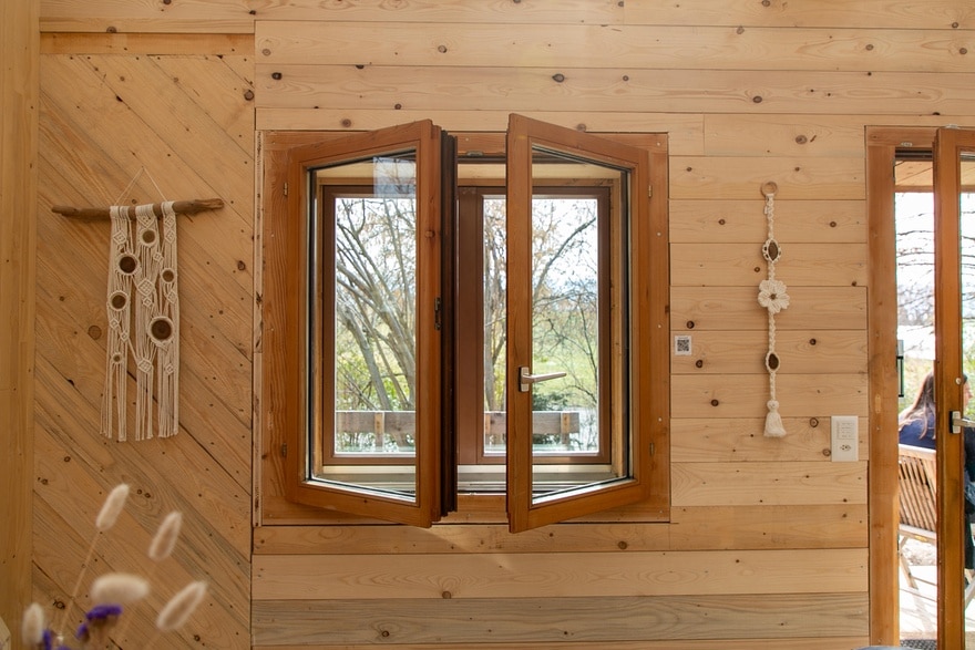 Blick auf eine Holzwand, mit einem doppelten Fenster, das nach innen leicht geöffnet ist. Die äussere Fensterfront ist geschlossen.